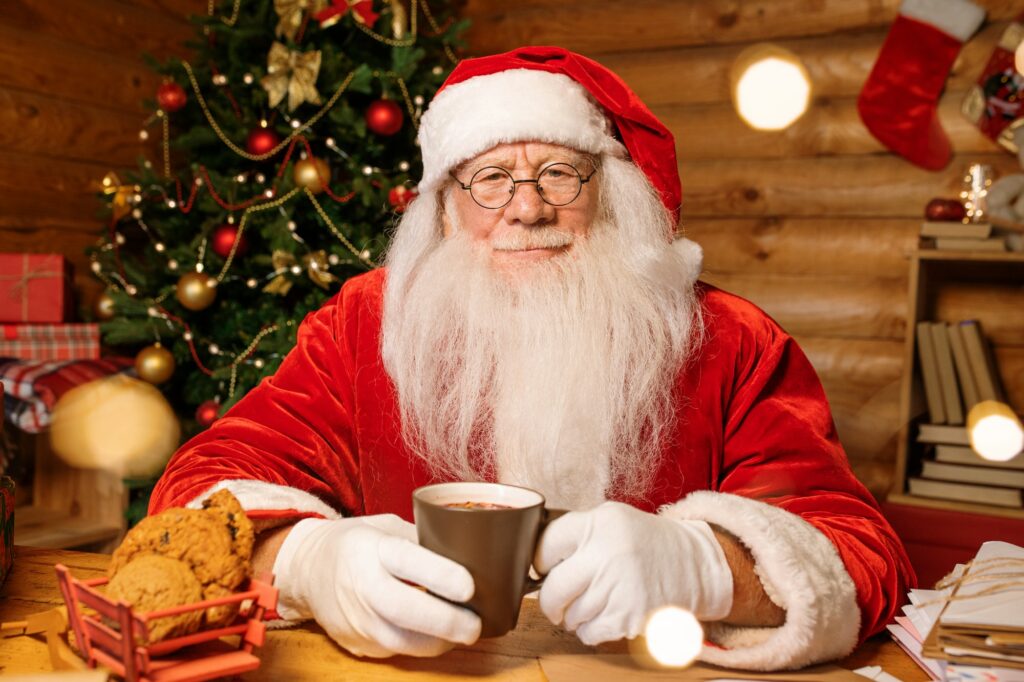 Santa with white beard having hot tea or coffee with fresh cookies by table
